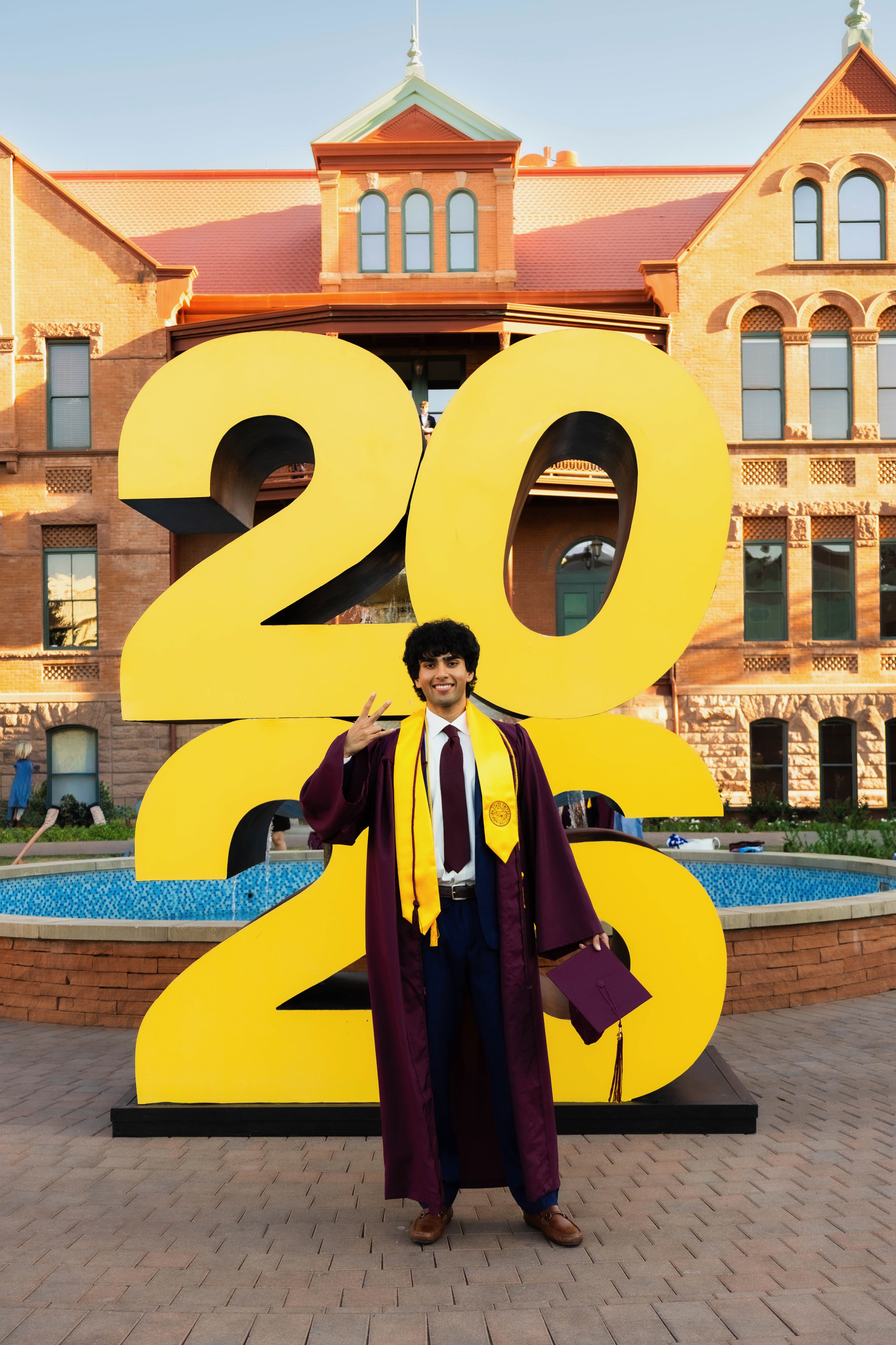 Yash making a peace sign in front of a giant "2026" sign at his ASU graduation.